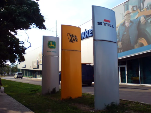 Stokkeri kolm reklaamposti John Deere'i, JCB ja Stilli brändidega parkla ääres