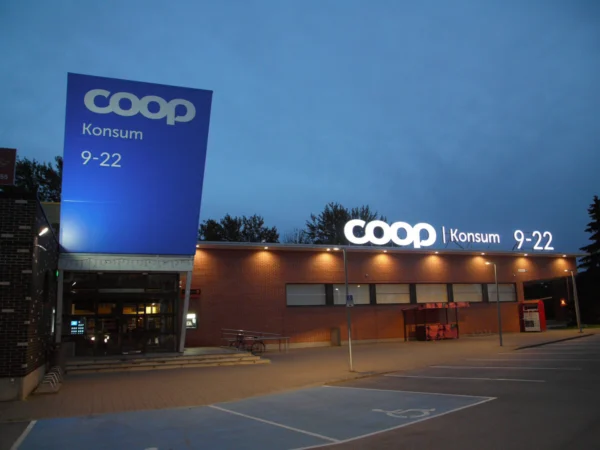 Coop Konsumi sinine valguskast sissepääsu juures ja valgustähtedega tekst hoone serval