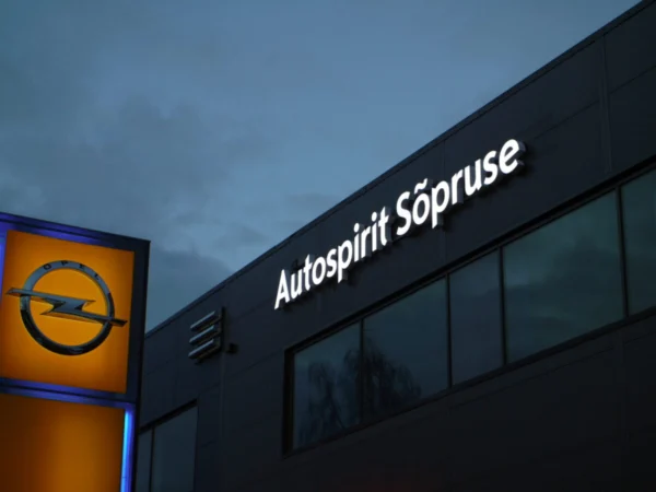 Autospirit Sõpruse valgustatud logo autoesinduse fassaadil koos Opeli pülonisildiga