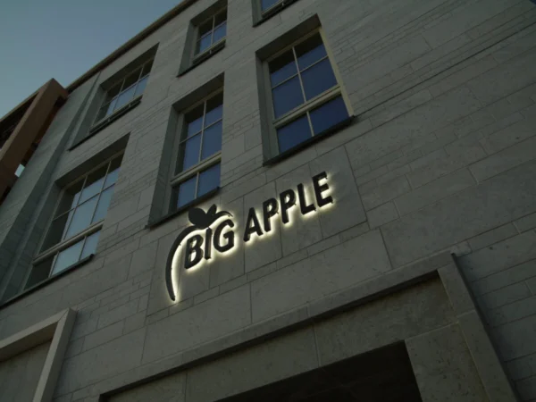Big Apple taustvalgustatud tähed hele-halli kivifassaadiga maja külje