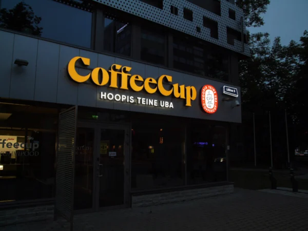 CoffeeCup kohviku valgustatud logo ja slogan ärihoone fassaadil õhtuhämaruses
