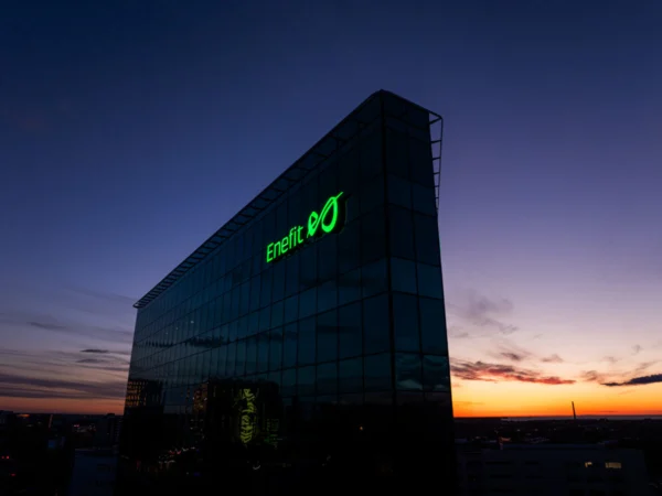 Enefiti roheline valgustatud logo klaasfassaadiga büroohoone tipus päikeseloojangul