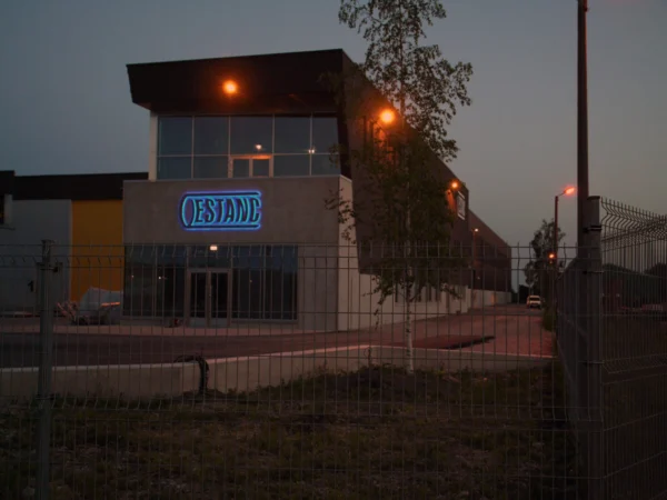ESTANC tootmishoone valgustatud logo halo-efektiga õhtuhämaruses
