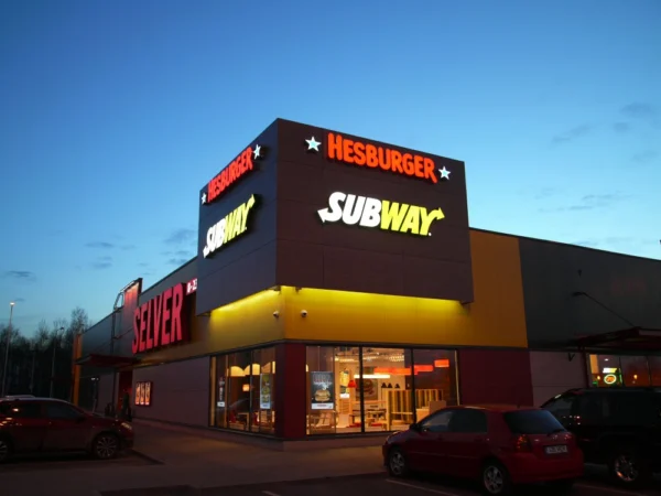 Subway ja Hesburgeri kiirtoidukoht Selveri juures, mitmed valgustatud bränded õhtuhämaruses