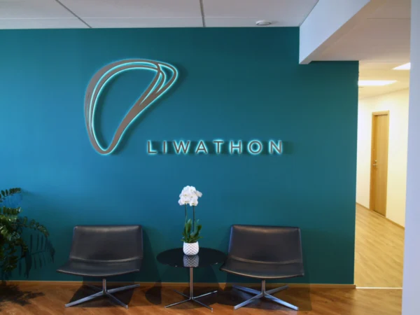 Liwathoni taustvalgustatud logo ja tekst kontori vastuvõtu tumerohelisel seinal