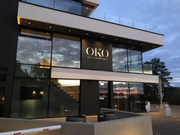 OKO Resto Haabneemes valgustatud logo restorani klaasfassaadil õhtuhämaruses