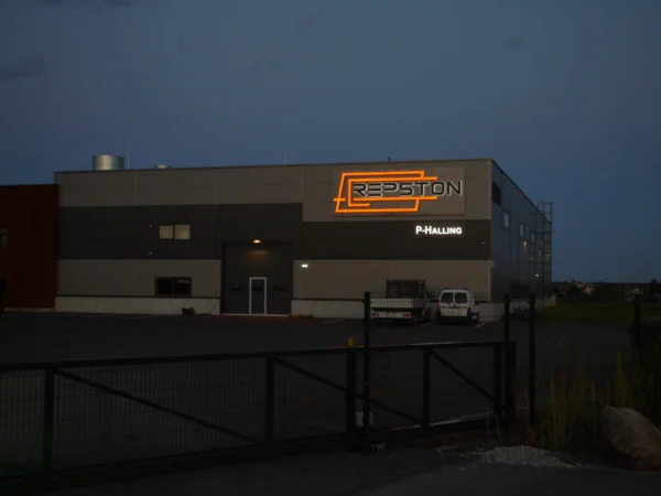Repstoni valgustatud logo oranži halo-efektiga laohoone tumehallil fassaadil