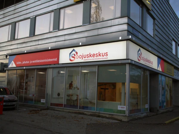 Soojuskeskus kaupluse valgustatud logo ja sloganibanner fassaadil