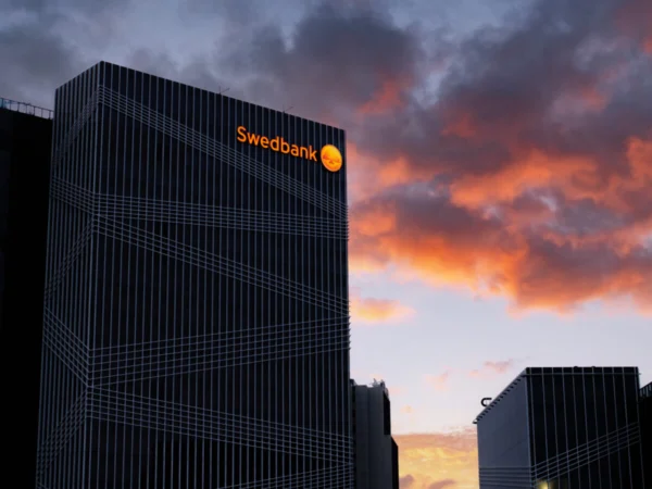 Swedbanki valgustatud logo kontorihoone katusel päikeseloojangu taustal
