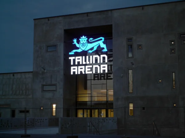 Tallinn Arena valgustatud lõvi-logo ja tekst tumehallil betoonfassaadil õhtuhämaruses