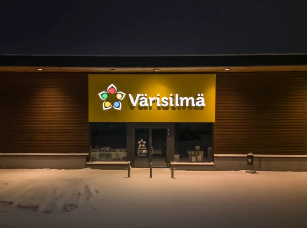 Värisilmä valgustatud logo kollasel fassaadipaneelil lumisel õhtul